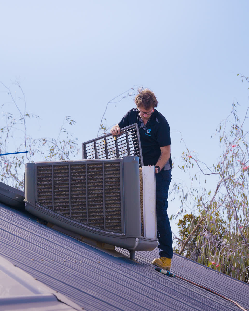 A Westplumb technician opening an evap unit on a dark roof