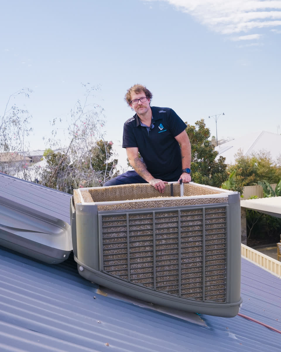 A Westplumb technician behind an evaporative cooler on a roof