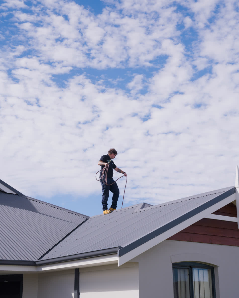 A Westplumb technician on a roof under a cloudy sky