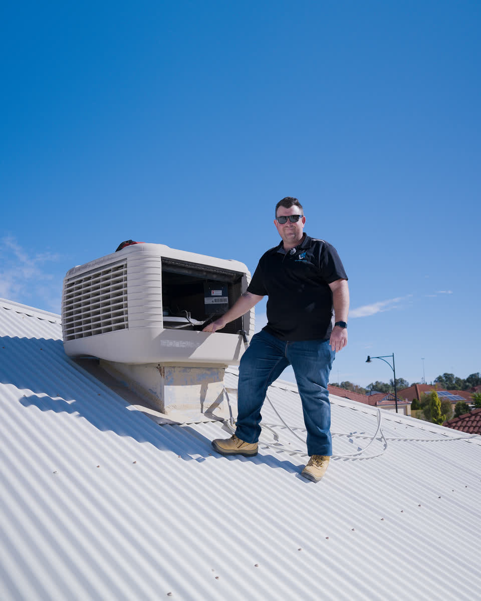 Brent standing beside an evaporative air conditioner on a roof