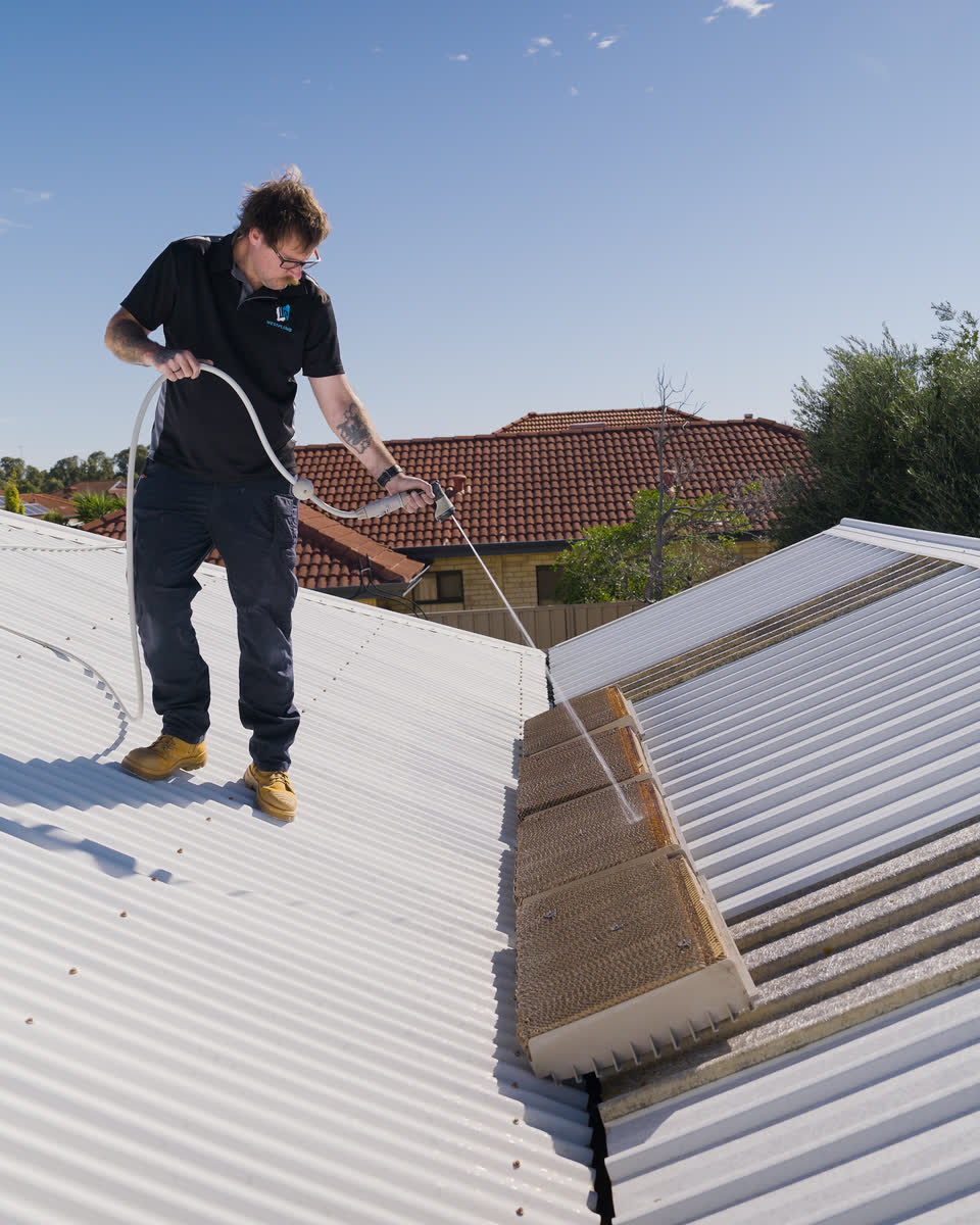 A Westplumb technician hosing evap cooling pads on a roof